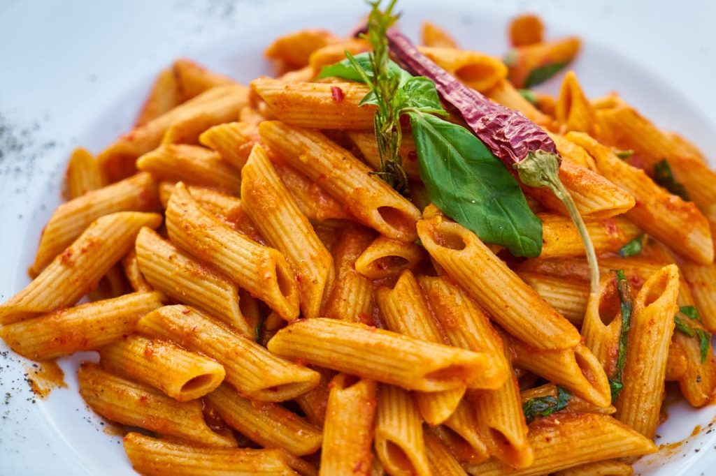 Delicious penne pasta with spicy red sauce, garnished with fresh basil and chili pepper.