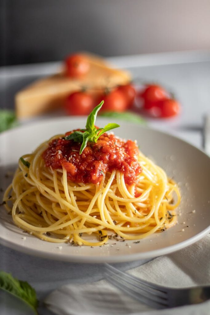 Appetizing spaghetti topped with tomato sauce and basil, served on a white plate.