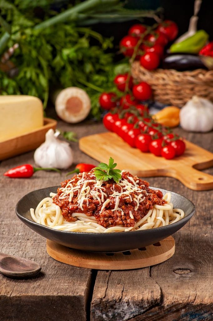 Delicious spaghetti bolognese topped with shredded cheese and fresh tomatoes in the background.